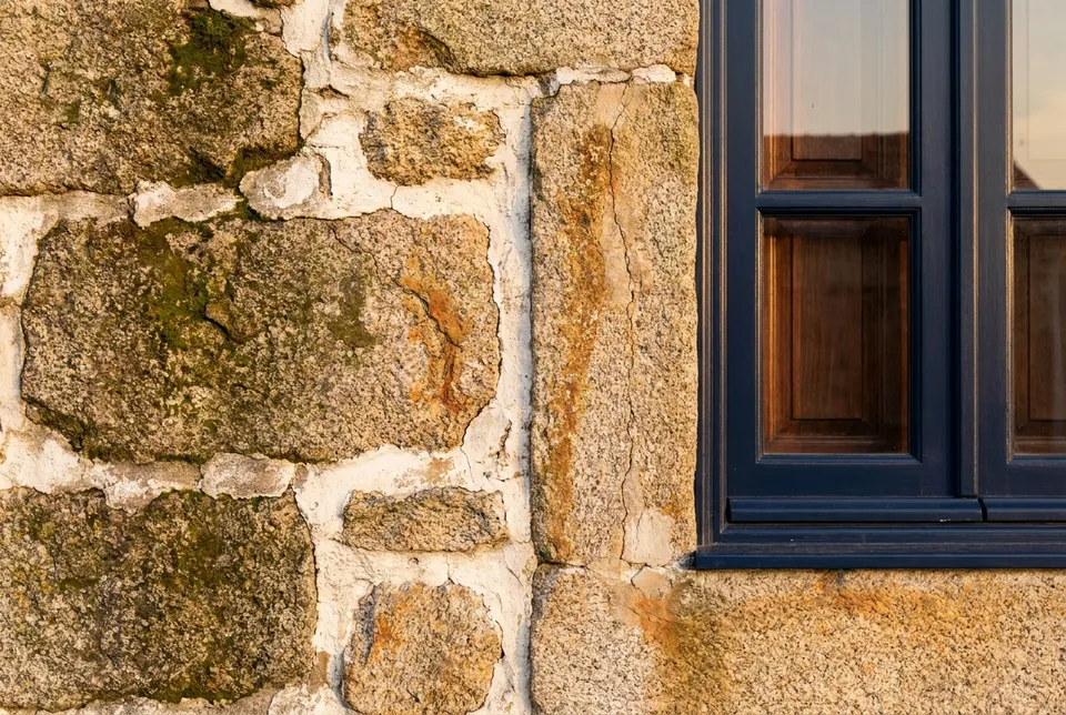 Detail of an old granite and lime wall next to a restored wooden window with a navy-blue frame